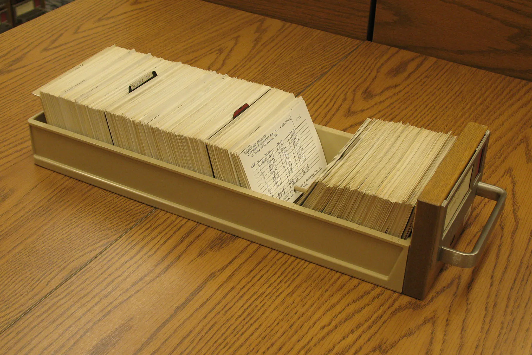 A drawer of index cards standing on a wooden table, one card pulled forward